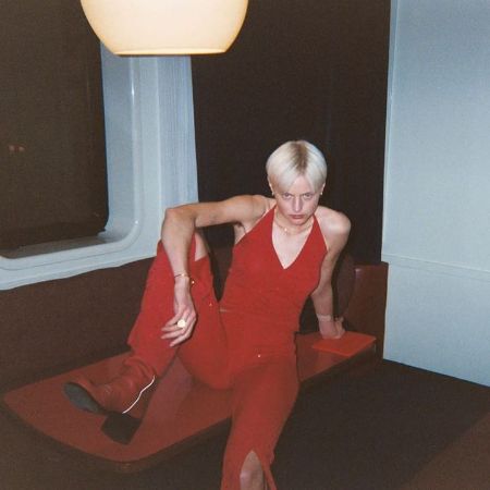 Emma Corrin is posing in a red dress.